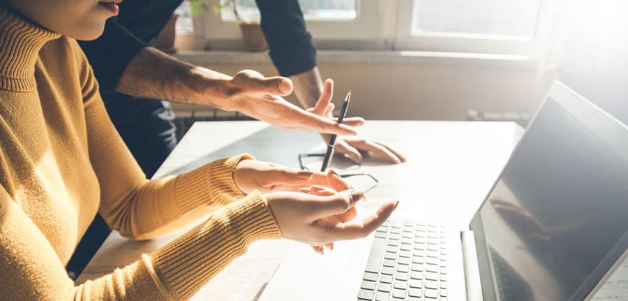 2 people in an office discussing work, looking at a laptop